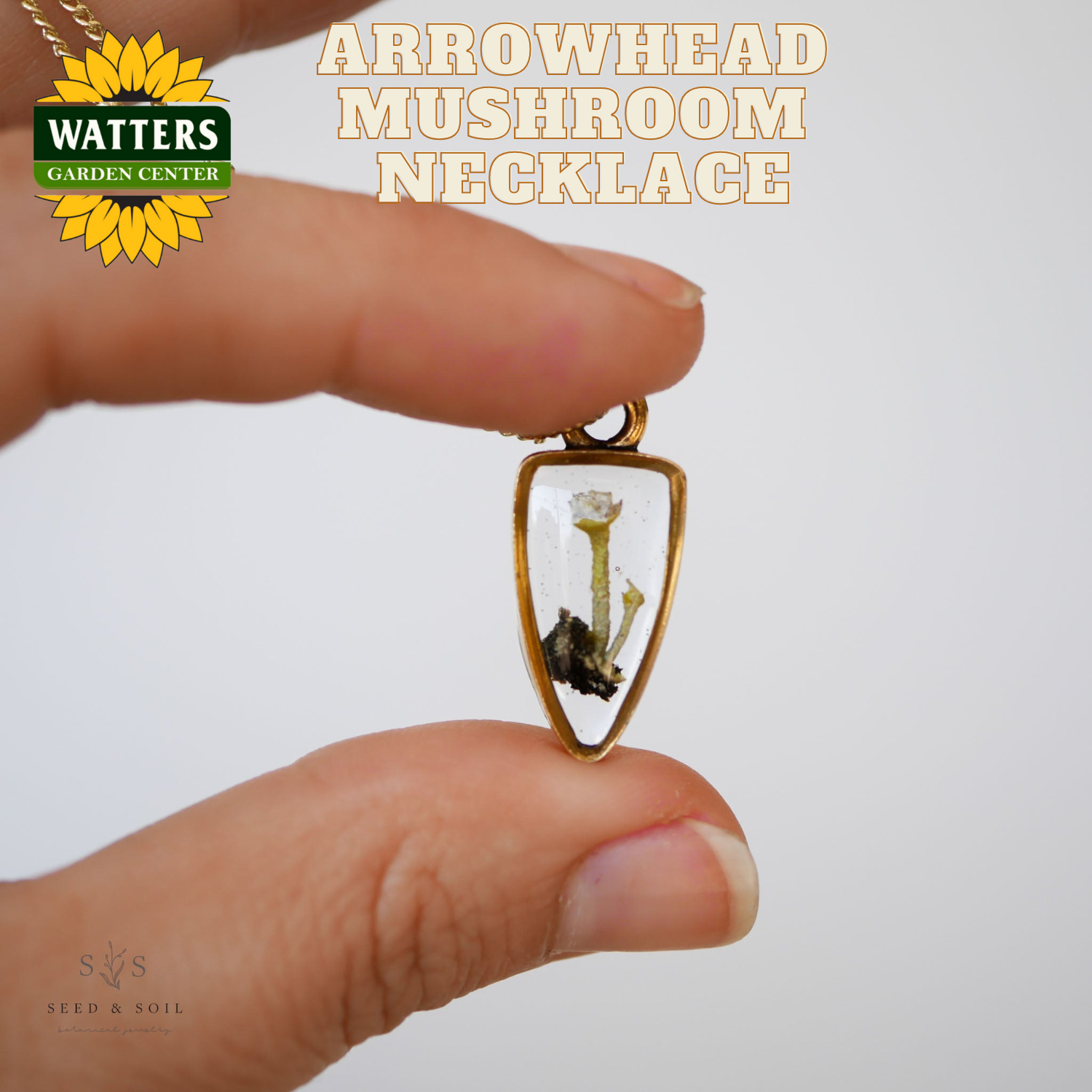Hand holding an arrowhead-shaped mushroom necklace with Watters Garden Center branding.