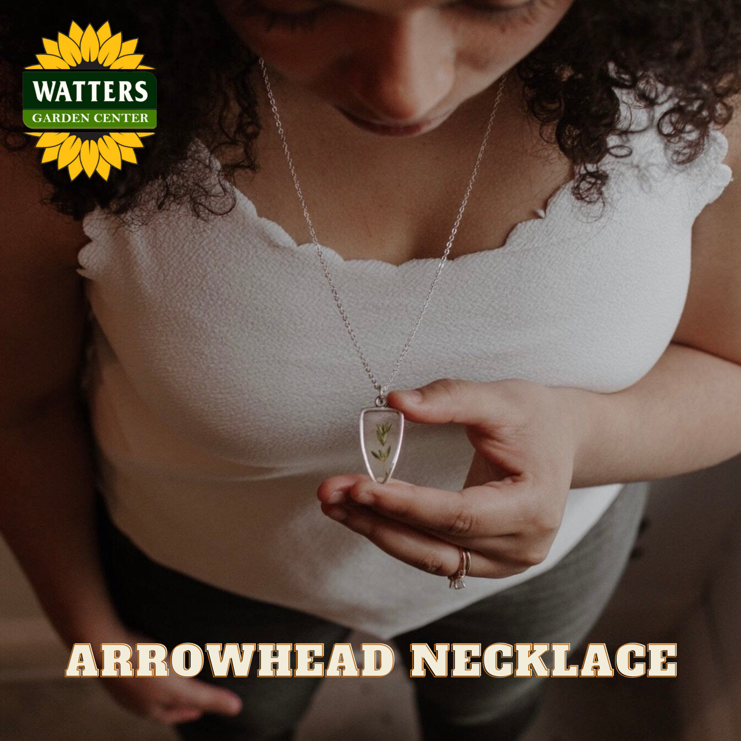 Person wearing a white top and holding an arrowhead necklace with Watters Garden Center branding.