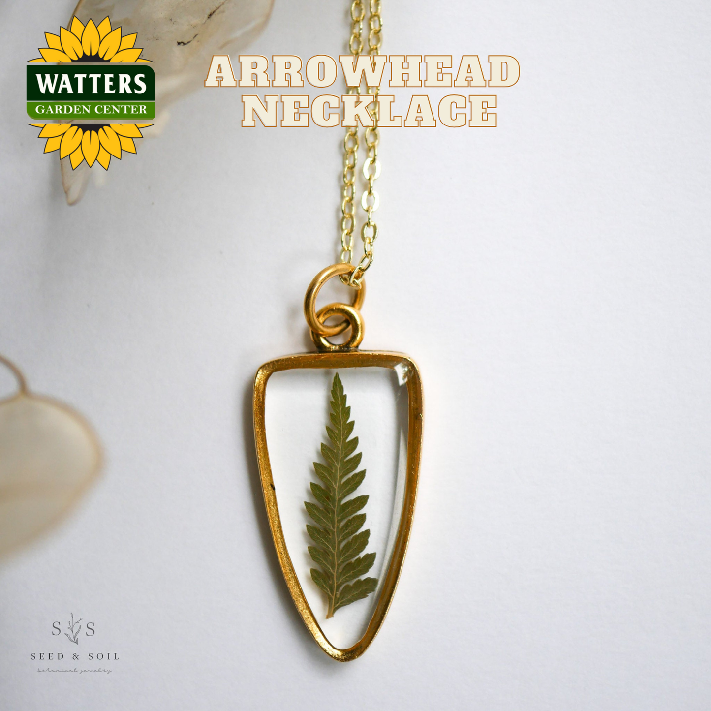 Gold arrowhead necklace with a leaf pendant on a white background, featuring Watters Garden Center logo.