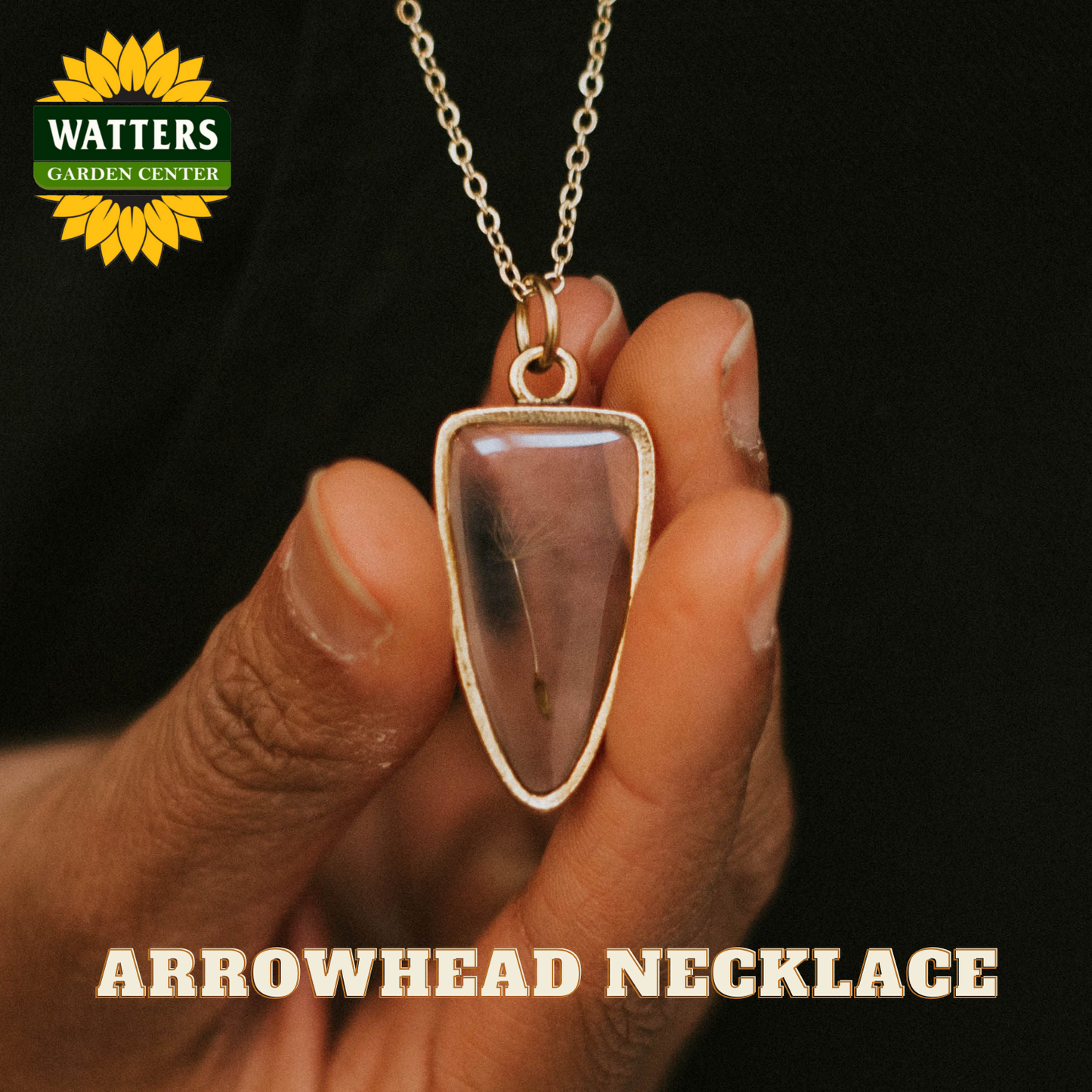 Hand holding an arrowhead necklace with Watters Garden Center logo.