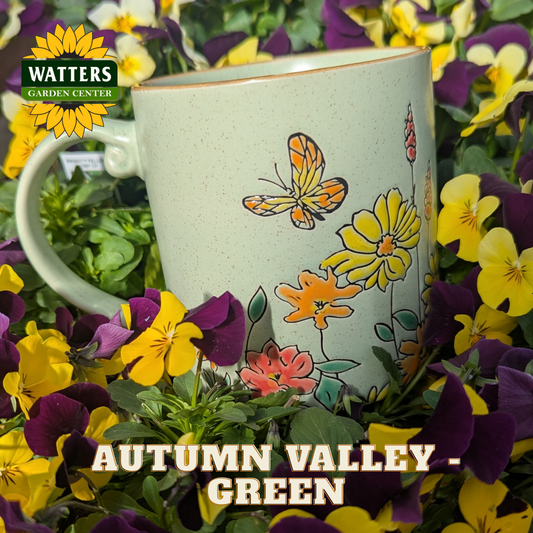 Butterfly and floral pattern on a green mug with purple and yellow flowers behind the Autumn Valley - Green mug with Watters logo.