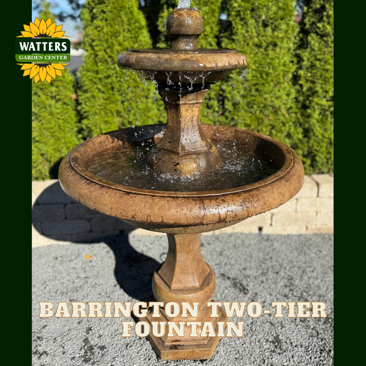 A two-tier outdoor stone fountain with water flowing from the top tier to the larger basin below, set on a gravel surface with green shrubs in the background. The Watters Garden Center logo appears in the top left, and the text 'BARRINGTON TWO-TIER FOUNTAIN' is overlaid at the bottom.