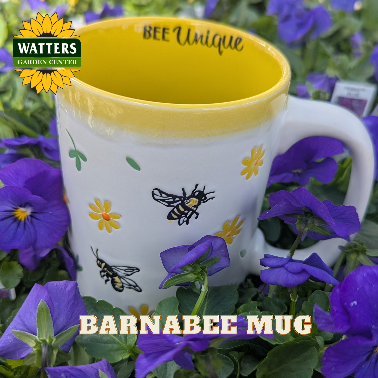 White mug with bee design and yellow interior, surrounded by purple flowers, Watters Garden Center logo visible.
