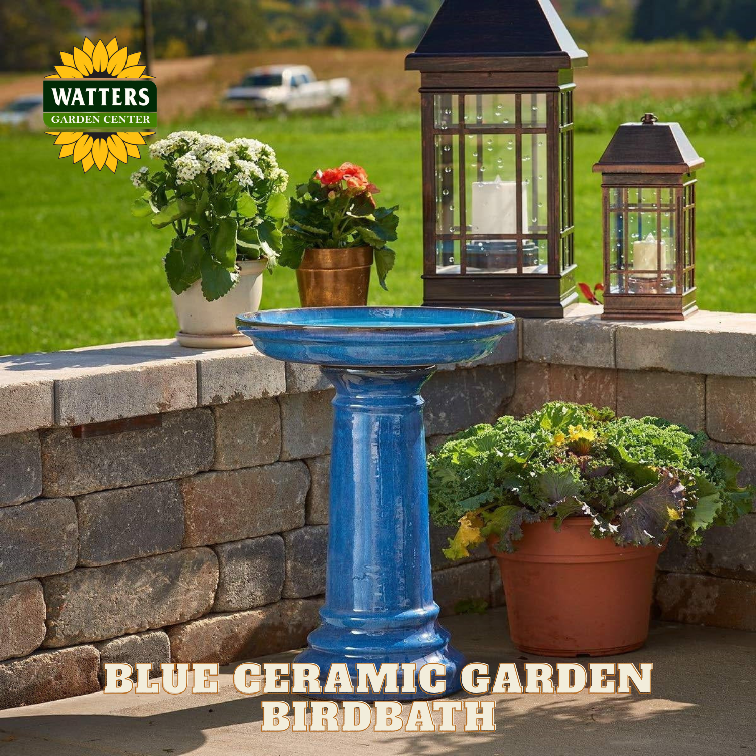 Blue ceramic garden birdbath with potted plants and lanterns on a stone ledge, Watters Garden Center logo visible.
