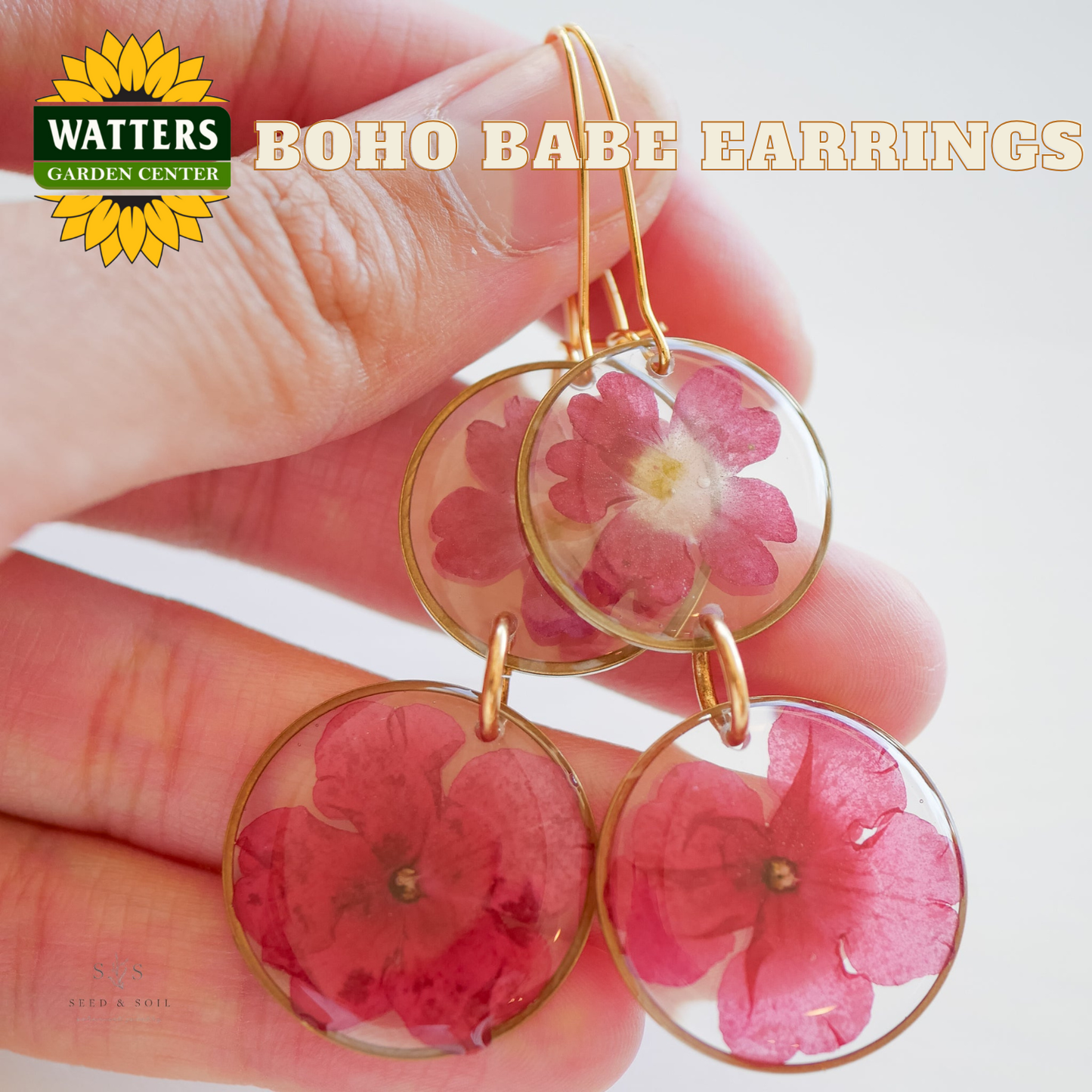 Boho Babe earrings with pink flowers held in a hand, Watters Garden Center branding visible.