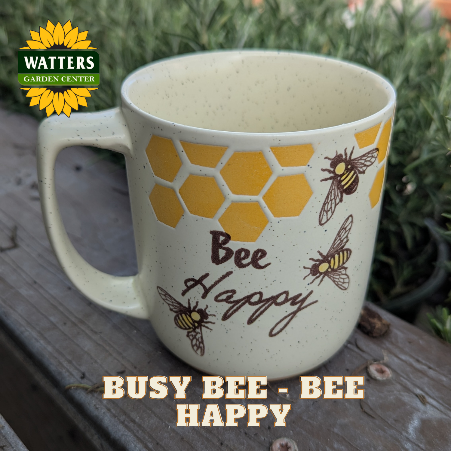 Mug with bee design and 'Bee Happy' text on a wooden surface, featuring Watters Garden Center logo.