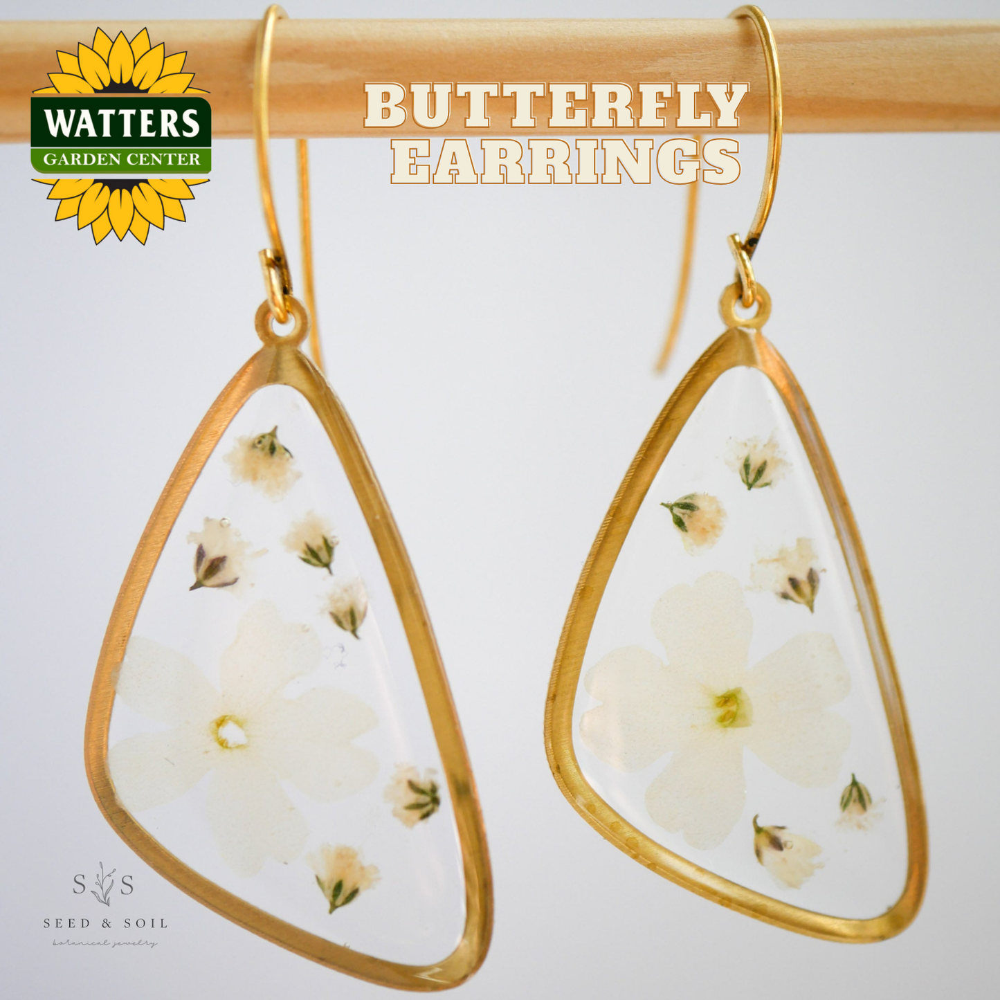 Butterfly earrings with gold frames and floral details on a white background, featuring Watters Garden Center branding.