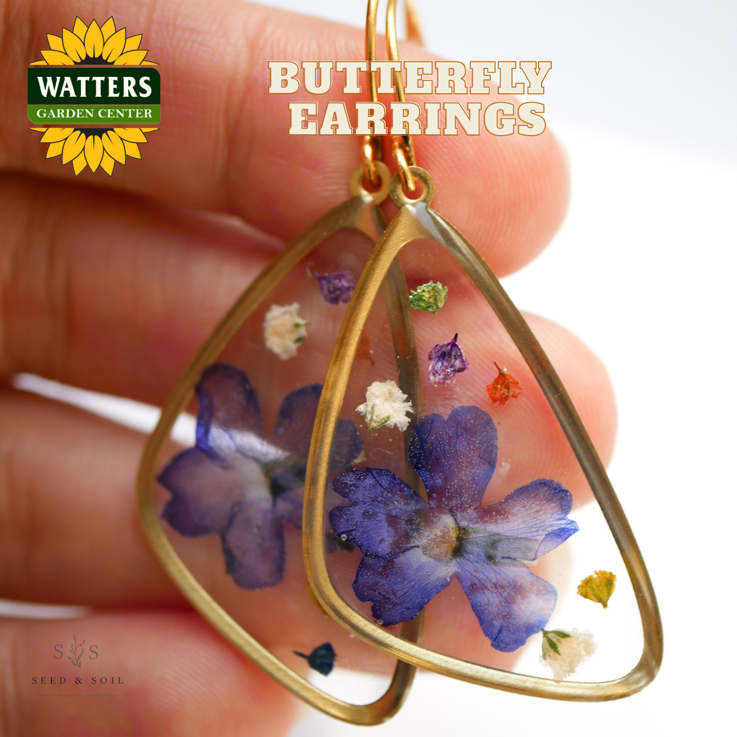 Butterfly earrings with pressed flowers held between fingers, Watters Garden Center logo visible.