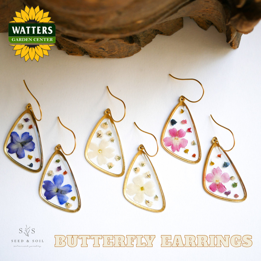 Butterfly earrings with floral designs on a white surface, featuring Watters Garden Center logo.