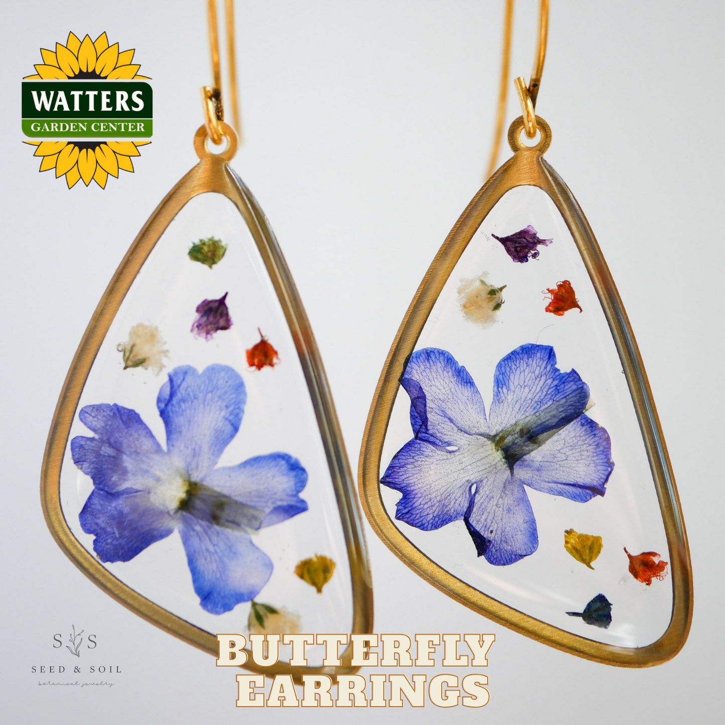 Butterfly earrings with pressed flowers in gold frames on a white background, featuring Watters Garden Center logo.