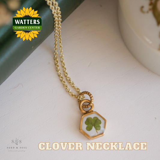 Gold necklace with a clover pendant on a white surface, featuring Watters Garden Center logo.
