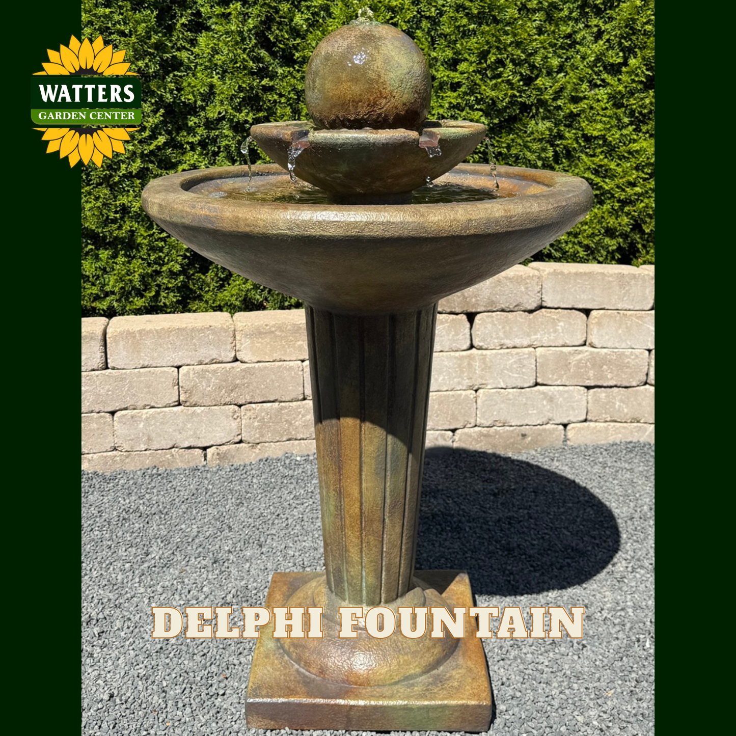 A DELPHI FOUNTAIN outdoor garden fountain with a bronze-toned pedestal base, wide shallow basin, and a spherical top bowl. The fountain is photographed outdoors on gravel in front of a stone wall and green hedges, with a WATTERS GARDEN CENTER logo in the top-left corner and DELPHI FOUNTAIN text at the bottom.