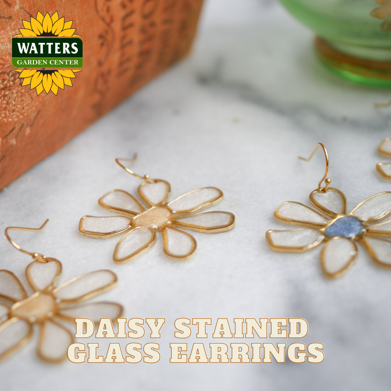 Daisy stained glass earrings on a marble surface with Watters Garden Center branding.