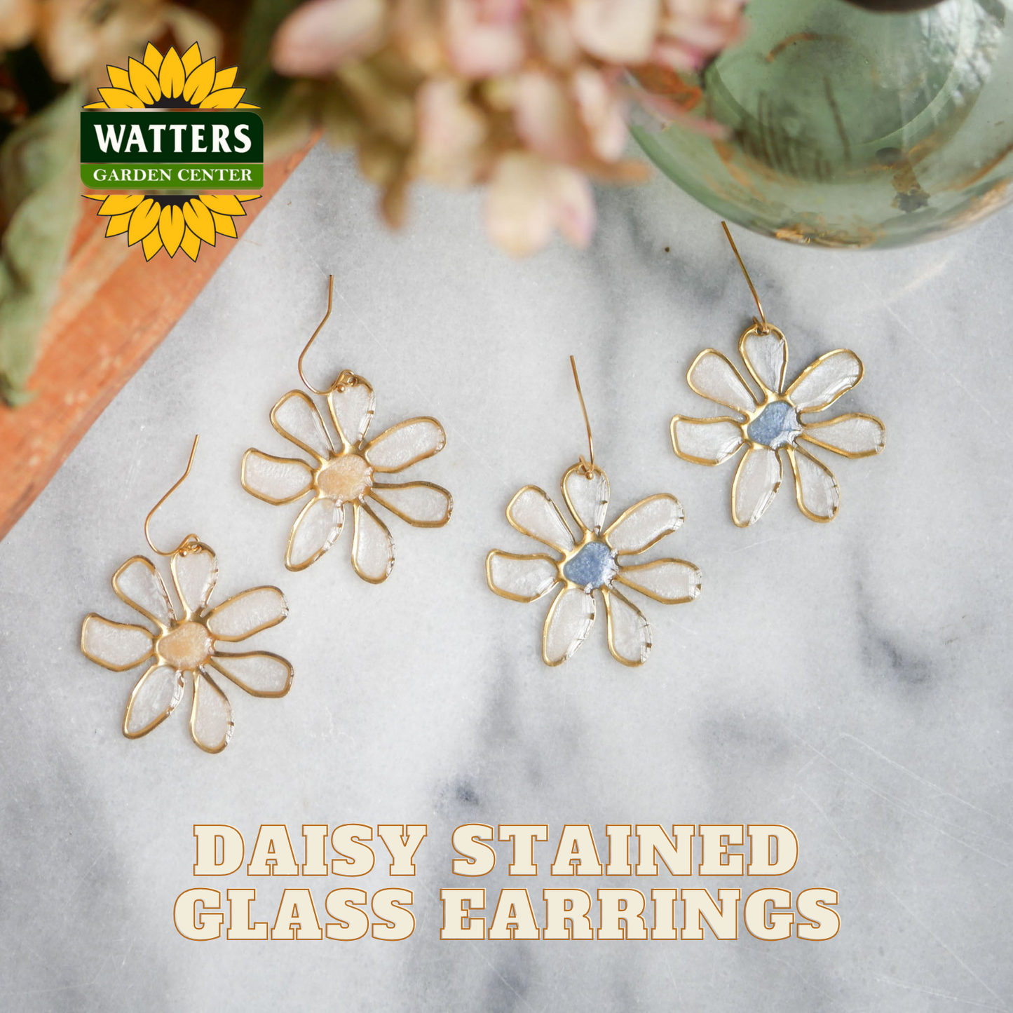 Gold daisy-stained glass earrings on a marble surface with Watters Garden Center logo.