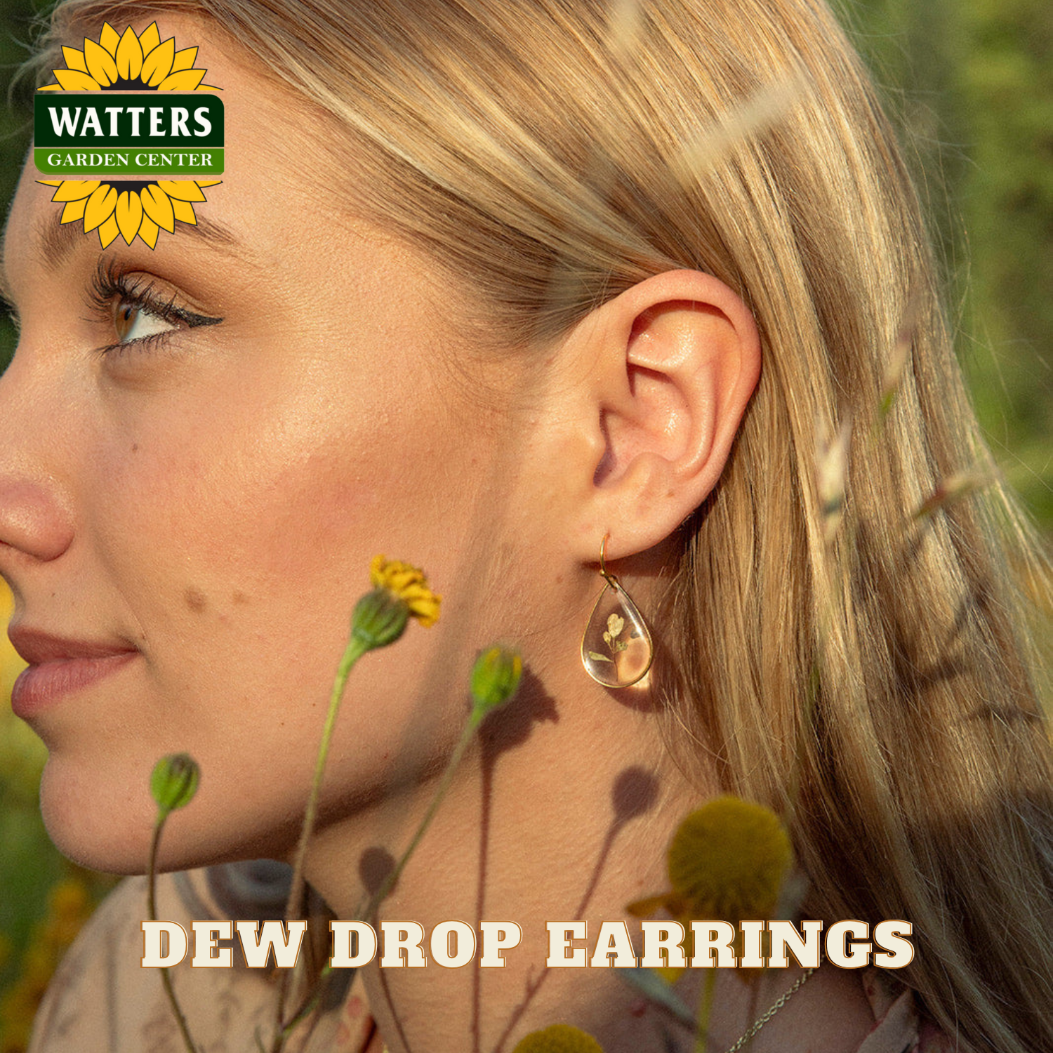Woman wearing Dew Drop earrings with a blurred natural background, featuring Watters Garden Center logo.