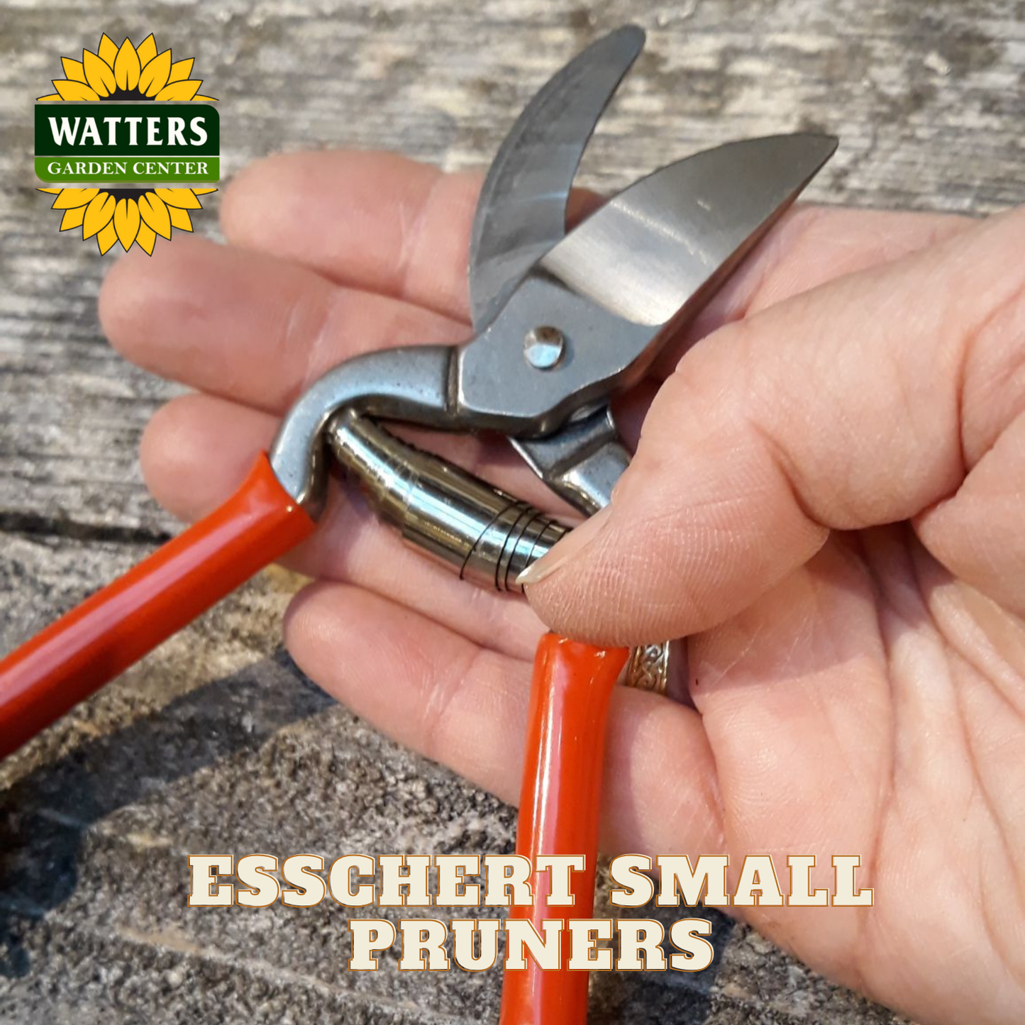 Red handled esschert pruners in a hand with Watters Garden Center Logo.