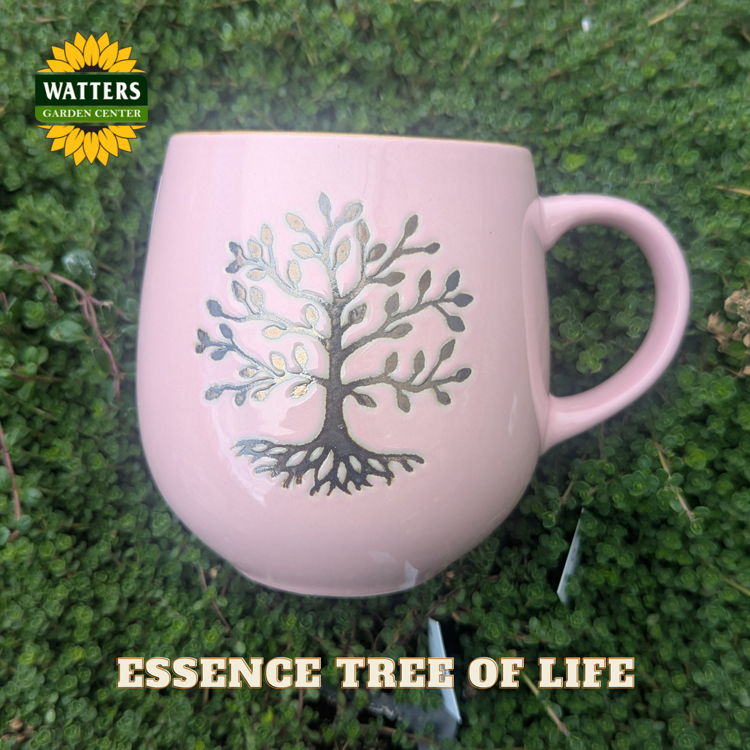 Pink mug with 'Essence Tree of Life' design on a green grass background, featuring Watters Garden Center logo.