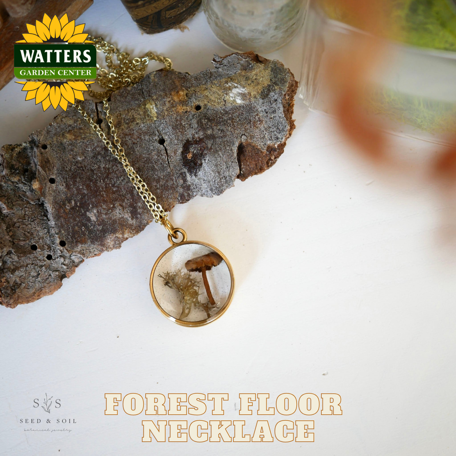 Gold necklace with a forest floor pendant on a rock, featuring Watters Garden Center branding.