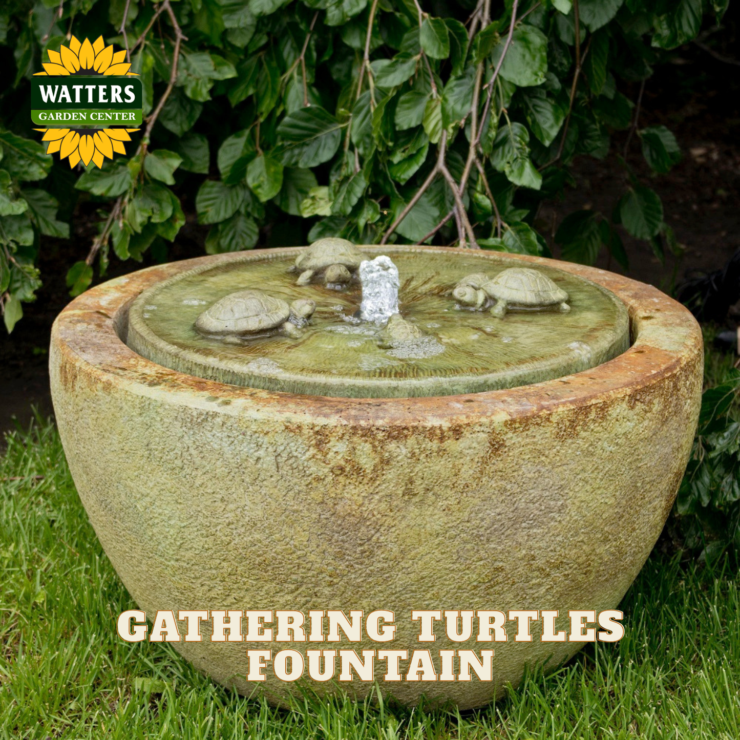 A round stone-style turtle fountain outdoors on grass with leafy plants behind it. The basin has a textured beige and green stone finish, a small central water feature, and turtle sculptures around the rim.
