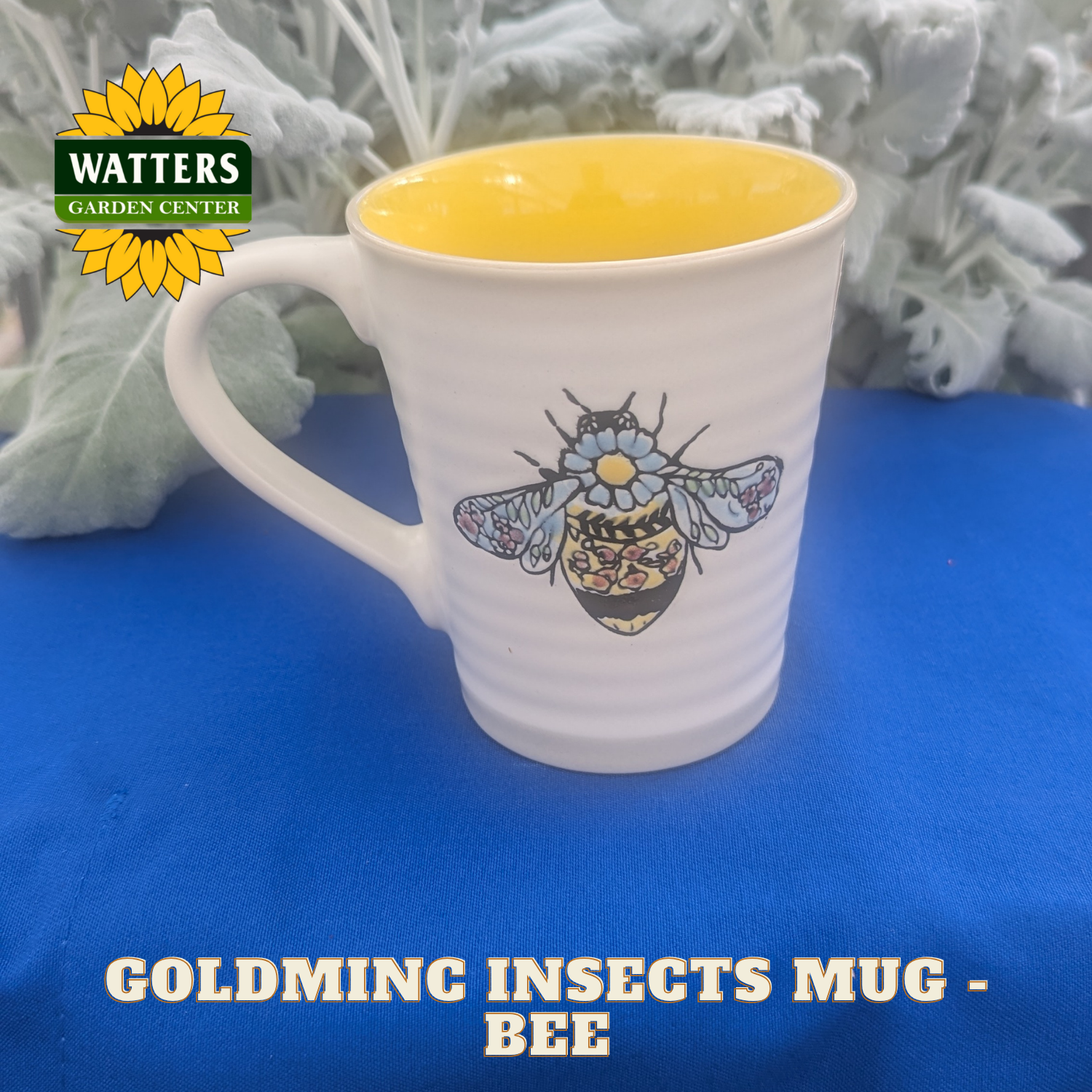 White mug with bee design on a blue surface, featuring Watters Garden Center logo.