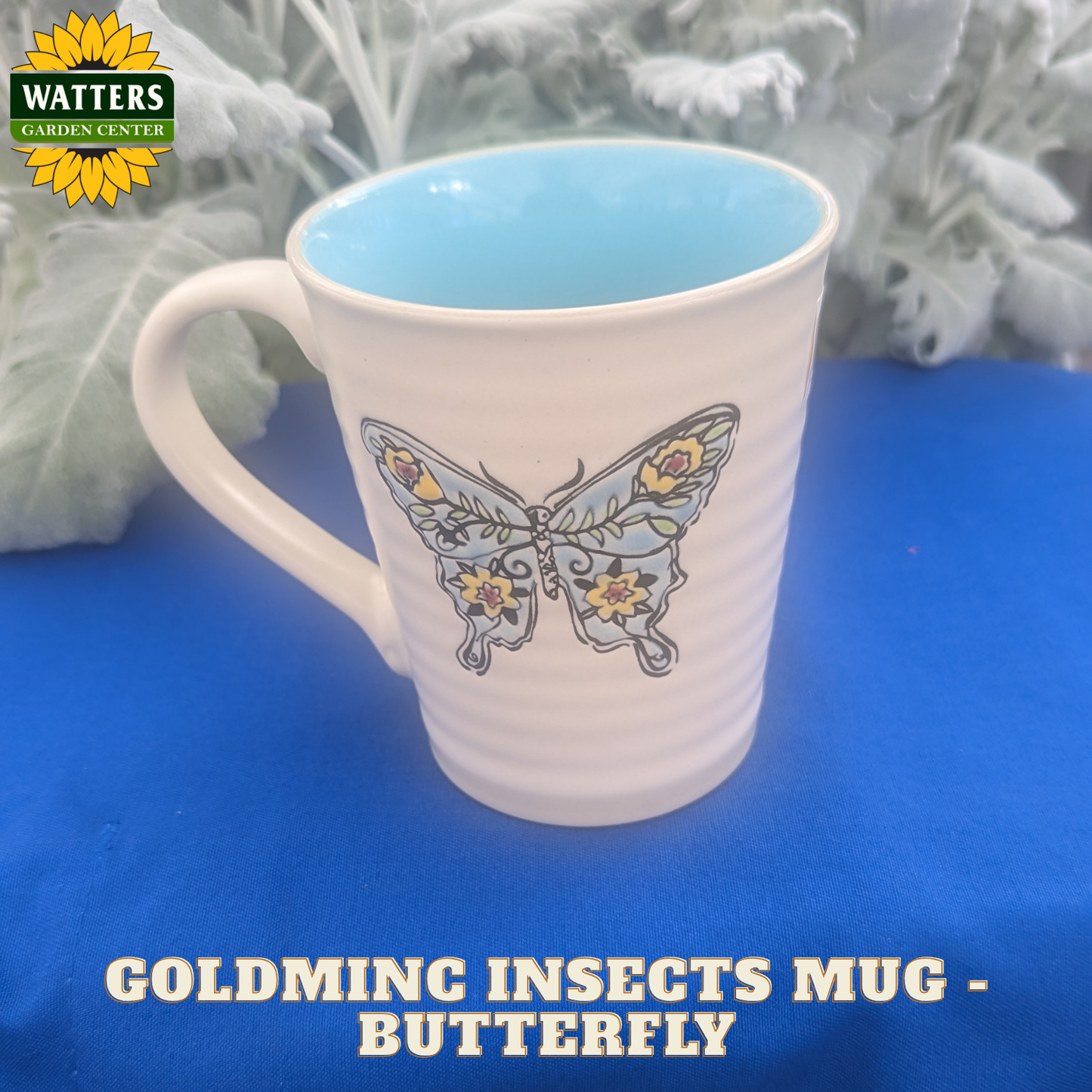 White mug with butterfly design on a blue surface, featuring Watters Garden Center logo.