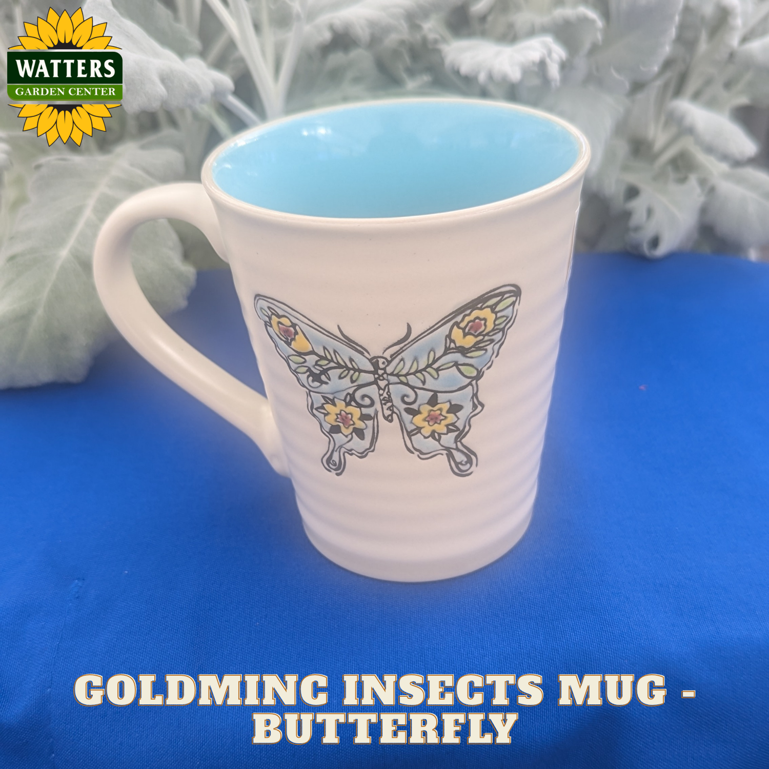 White mug with butterfly design on a blue surface, featuring Watters Garden Center logo.