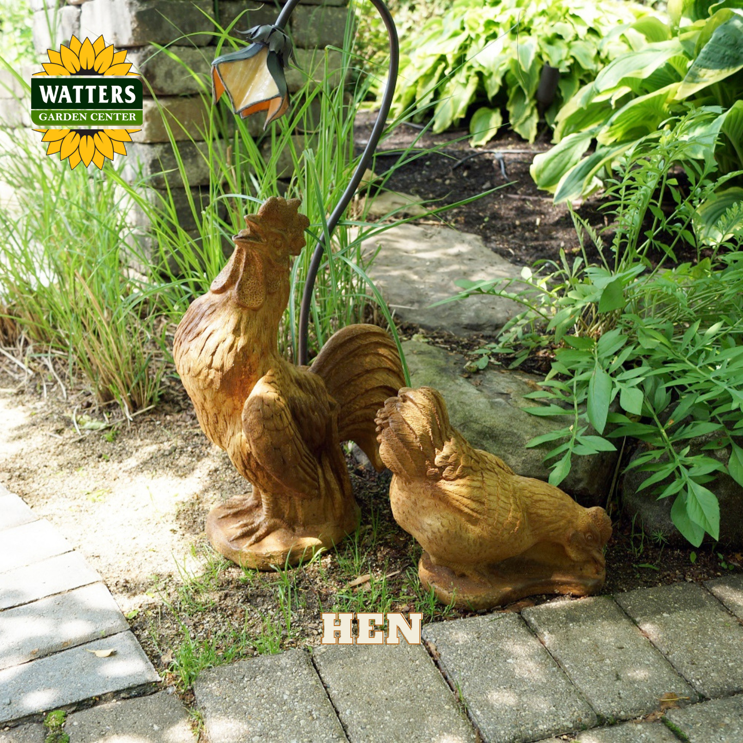 Two rustic wooden chicken garden statues, labeled 'HEN', placed on a stone path in a garden setting. One is a rooster and one is a hen, both in a warm brown finish.