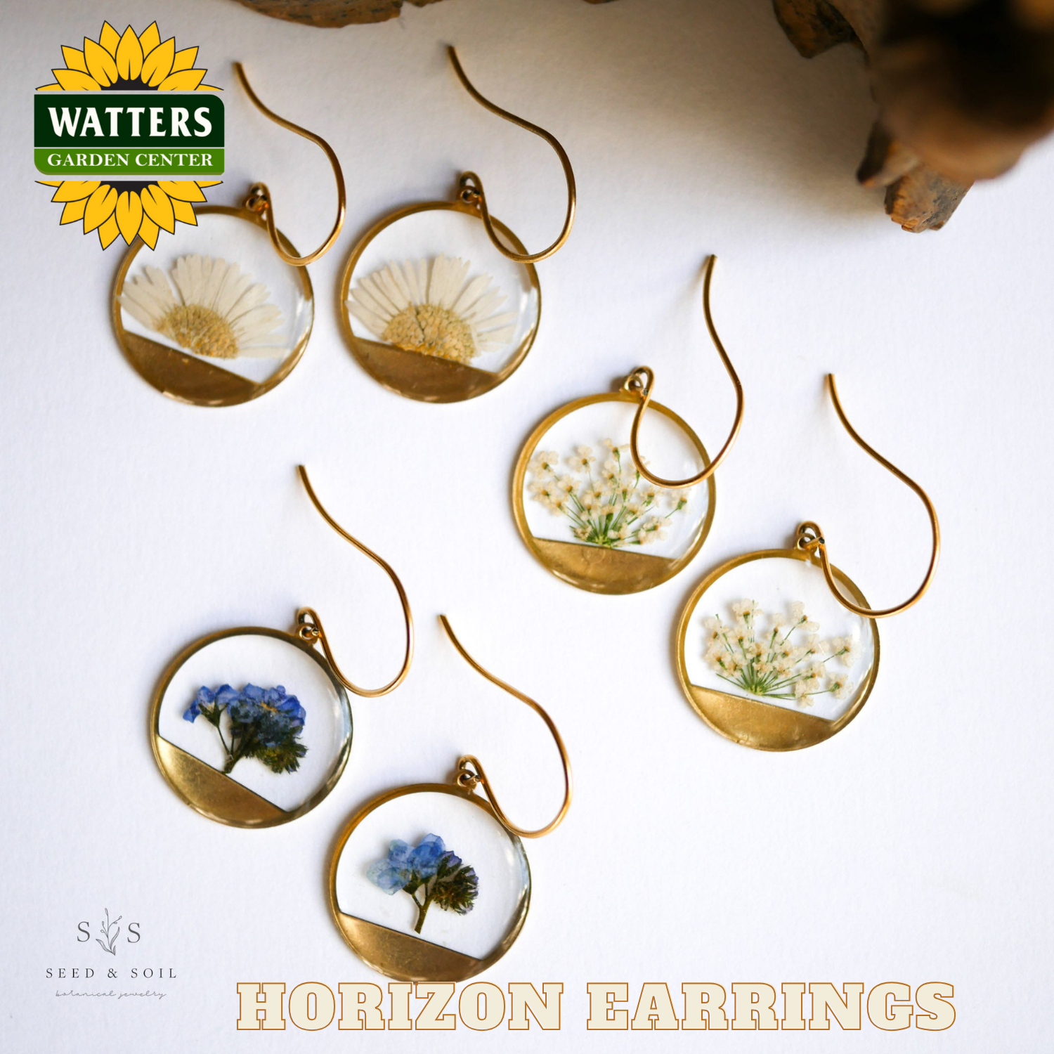 Gold earrings with embedded flowers on a white surface, featuring Watters Garden Center branding.