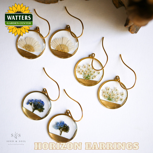 Gold earrings with embedded flowers on a white surface, featuring Watters Garden Center branding.