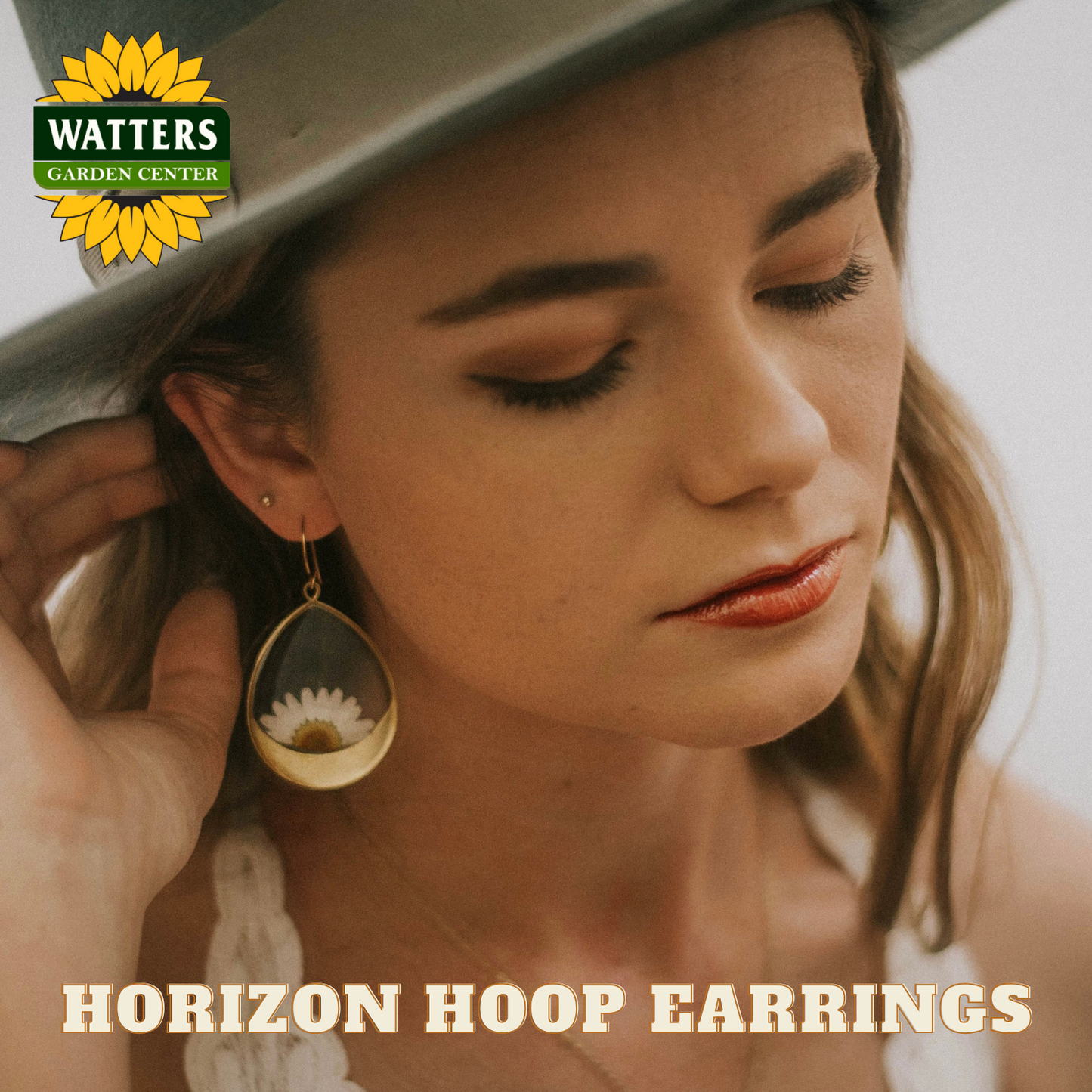 Woman wearing a 'Horizon Hoop Earrings' with Watters Garden Center branding.
