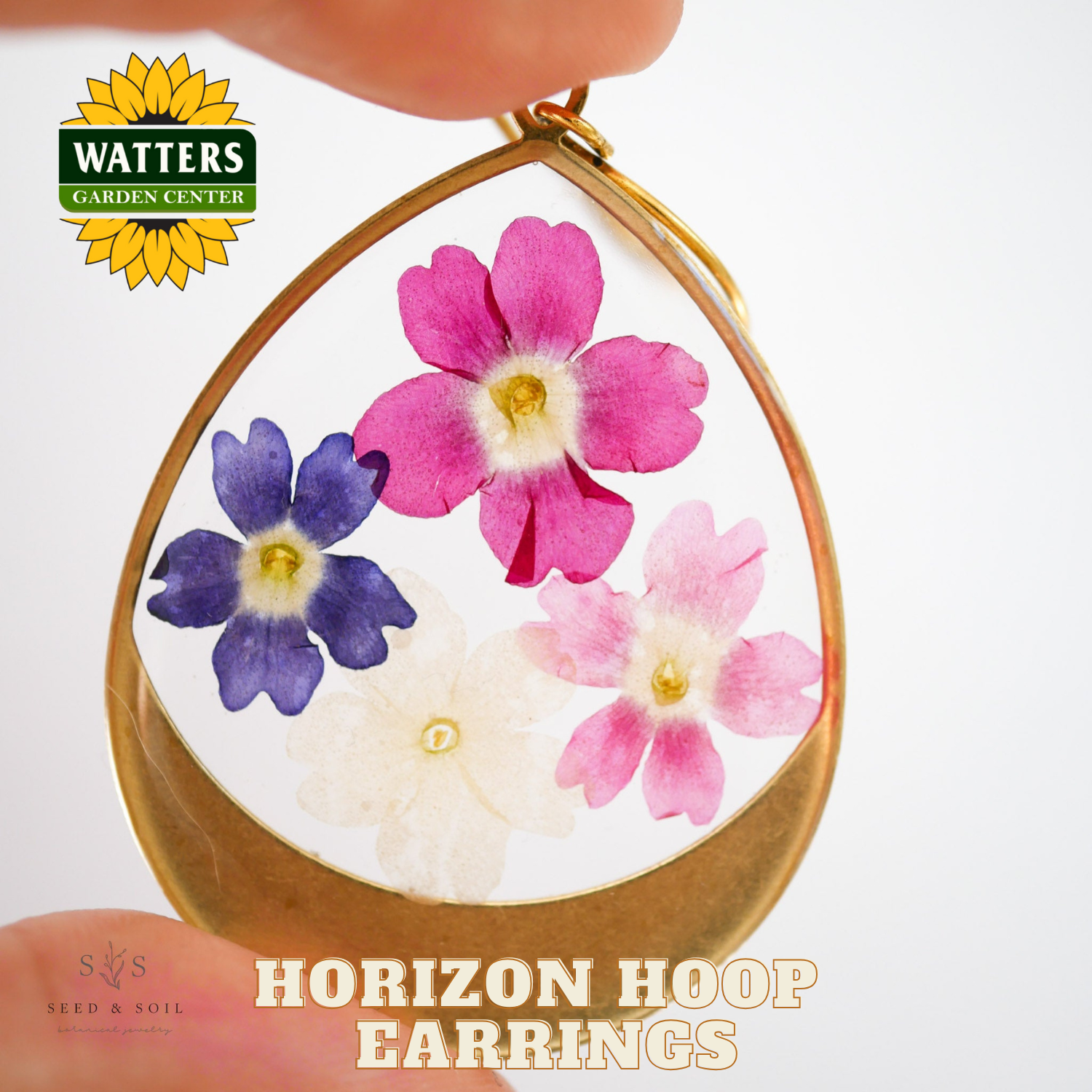 Horizon hoop earrings with flowers held by a hand, Watters Garden Center logo visible.