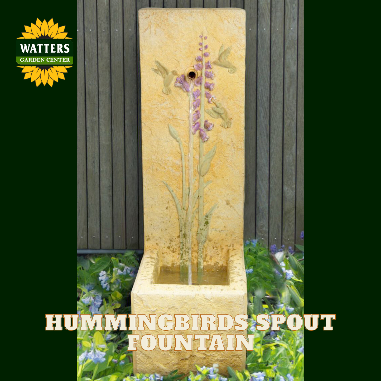 A tall rectangular stone fountain with a hummingbird spout, shown outdoors against a dark wooden fence and garden plants. The fountain has a warm beige stone finish with painted purple flowers and green stems.