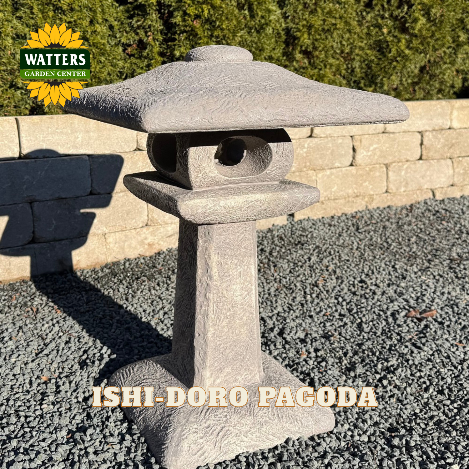 A gray stone lantern garden light shaped like an ishido pagoda, shown outdoors on a bed of gravel in front of a stone wall and green shrubs. A Watters Garden Center logo is visible in the top left, and 'ISHI-DORO PAGODA' is written across the bottom.