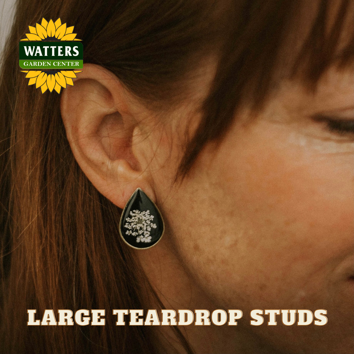 Close-up of an ear wearing a large teardrop stud earring with Watters Garden Center logo.