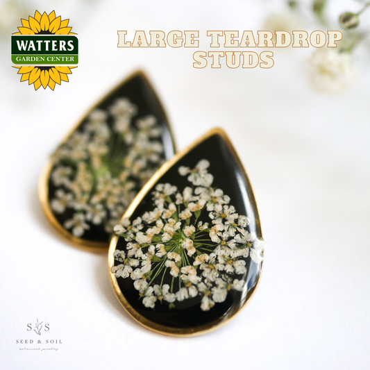 Black teardrop earrings with white floral design on a light background, featuring Watters Garden Center logo.