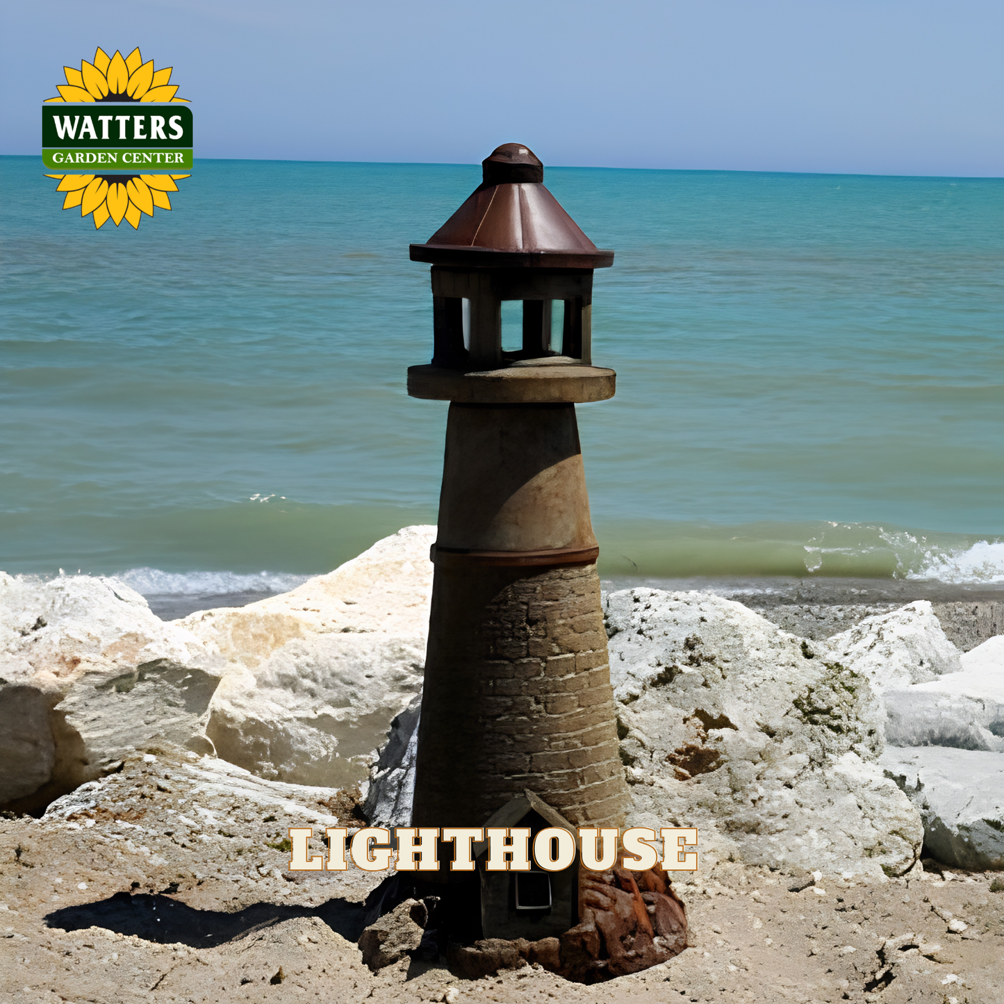 A decorative metal lighthouse garden statue stands on a sandy beach with rocks and the ocean in the background. The Watters Garden Center logo is in the top-left corner, and the word 'LIGHTHOUSE' is overlaid at the bottom.