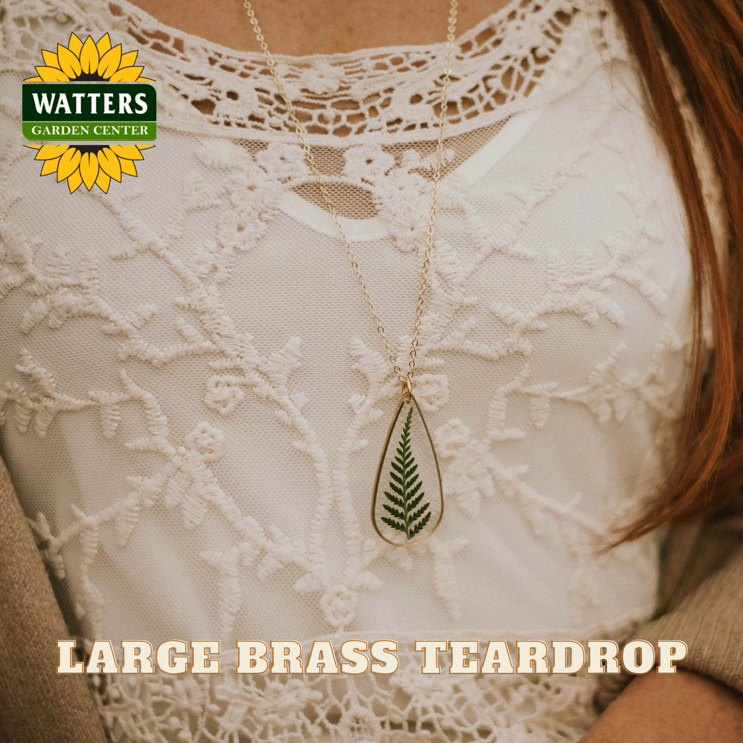 Necklace with a large brass teardrop pendant featuring a leaf design, worn on a lace garment with Watters Garden Center logo.