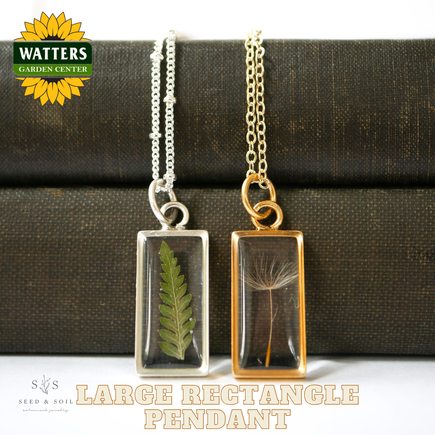 Two necklaces with rectangular pendants featuring pressed leaves, one silver and one gold, on a textured surface with Watters Garden Center branding.