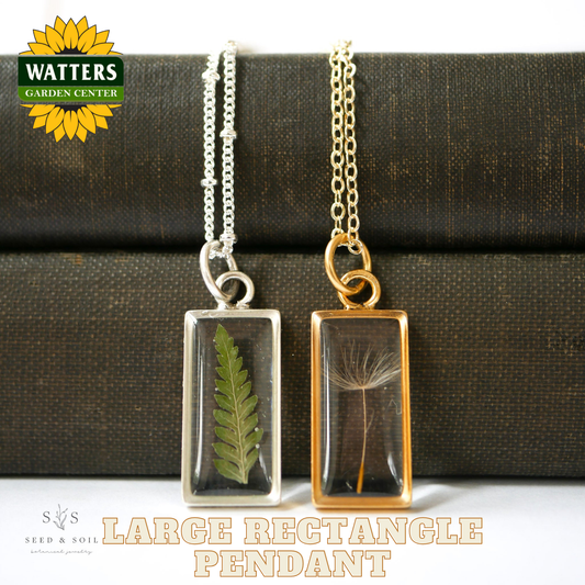 Two necklaces with rectangular pendants featuring pressed leaves, one silver and one gold, on a textured surface with Watters Garden Center branding.