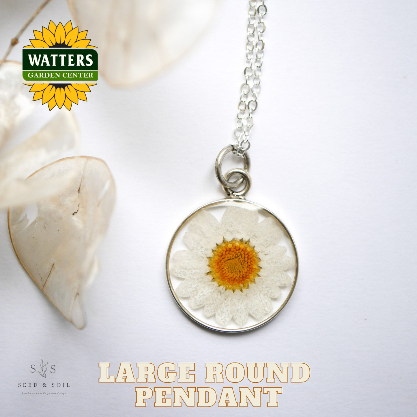 Large round pendant with a pressed flower on a white background, featuring Watters Garden Center logo.