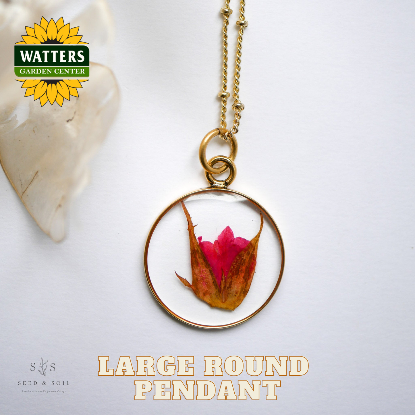 Gold pendant with a pink flower on a white background, featuring Watters Garden Center logo.