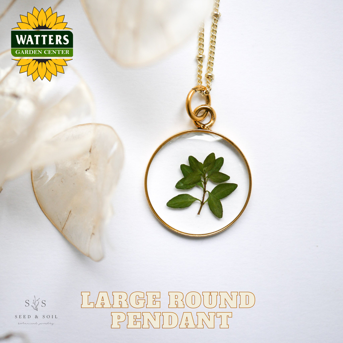 Gold pendant with green leaf design on a white background, featuring Watters Garden Center logo.