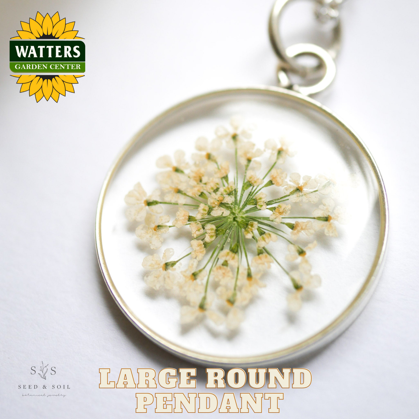 Large round pendant with pressed flowers on a white background, featuring Watters Garden Center logo.