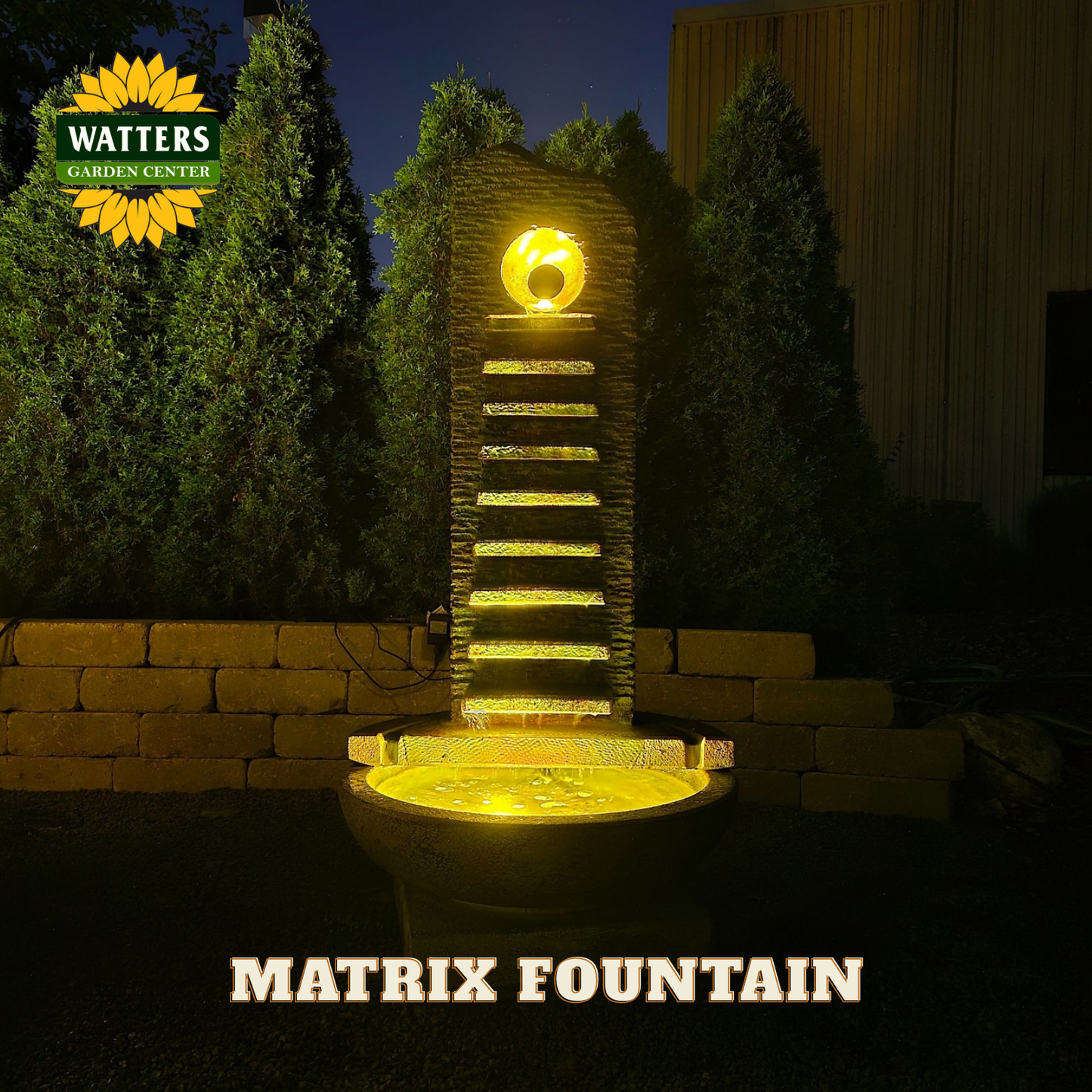 Decorative fountain with illuminated design at night, branded 'Watters Garden Center'.