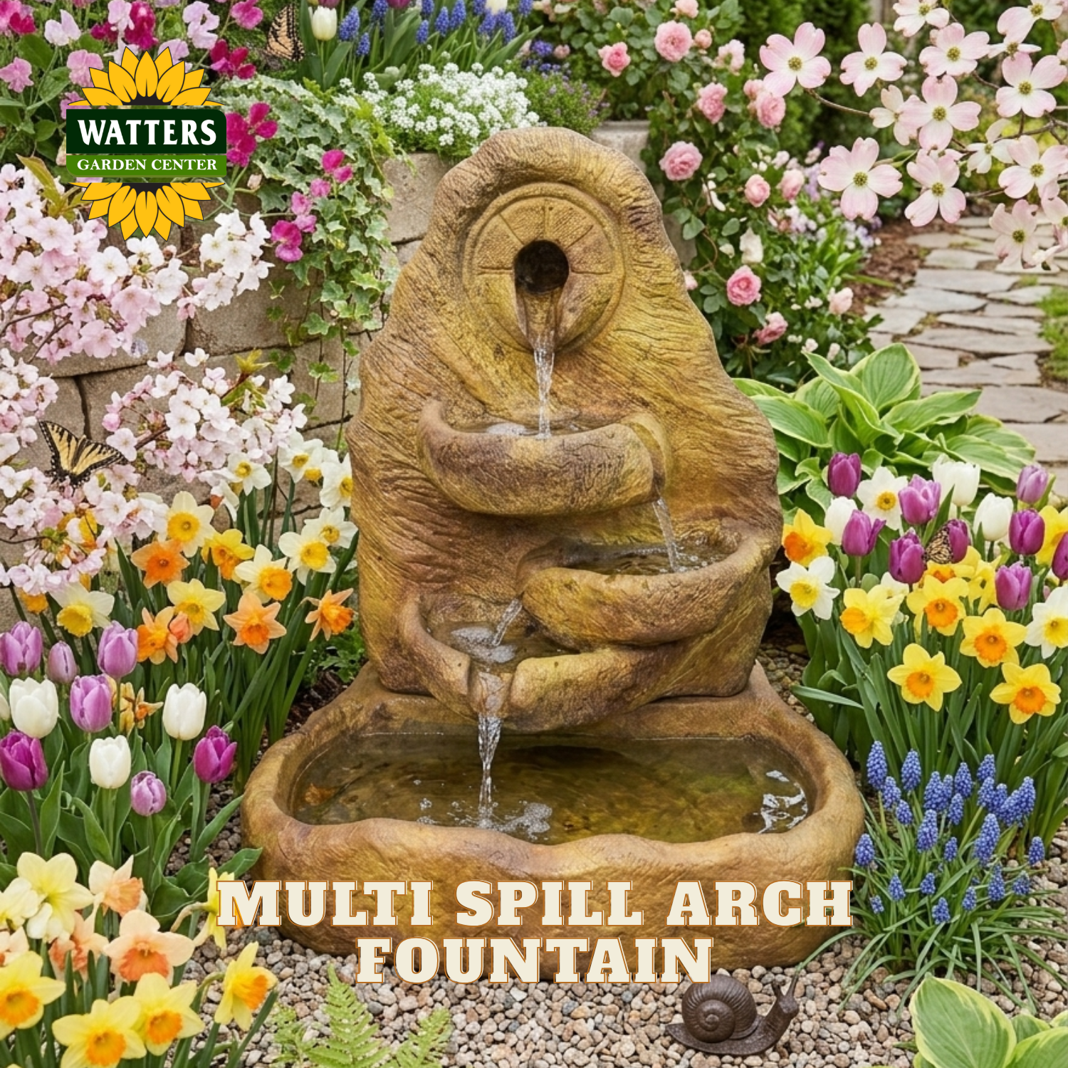A Watters Gardens Center multi spill arch fountain made of textured stone in a warm tan-brown color, set in a lush garden with colorful flowers and water cascading into a basin below.