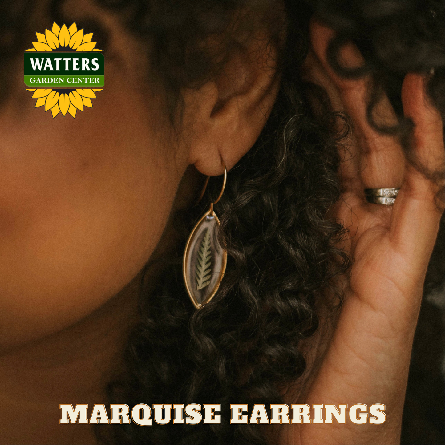 Close-up of a person wearing marquise earrings with Watters Garden Center logo.