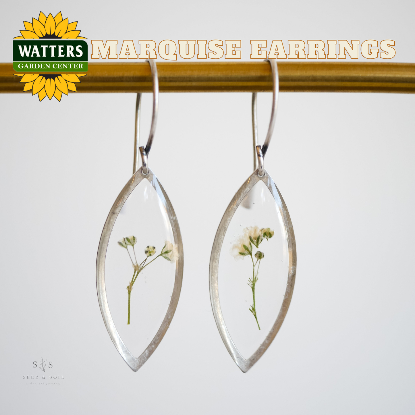Silver marquise earrings with pressed flowers on a white background, featuring Watters Garden Center branding.