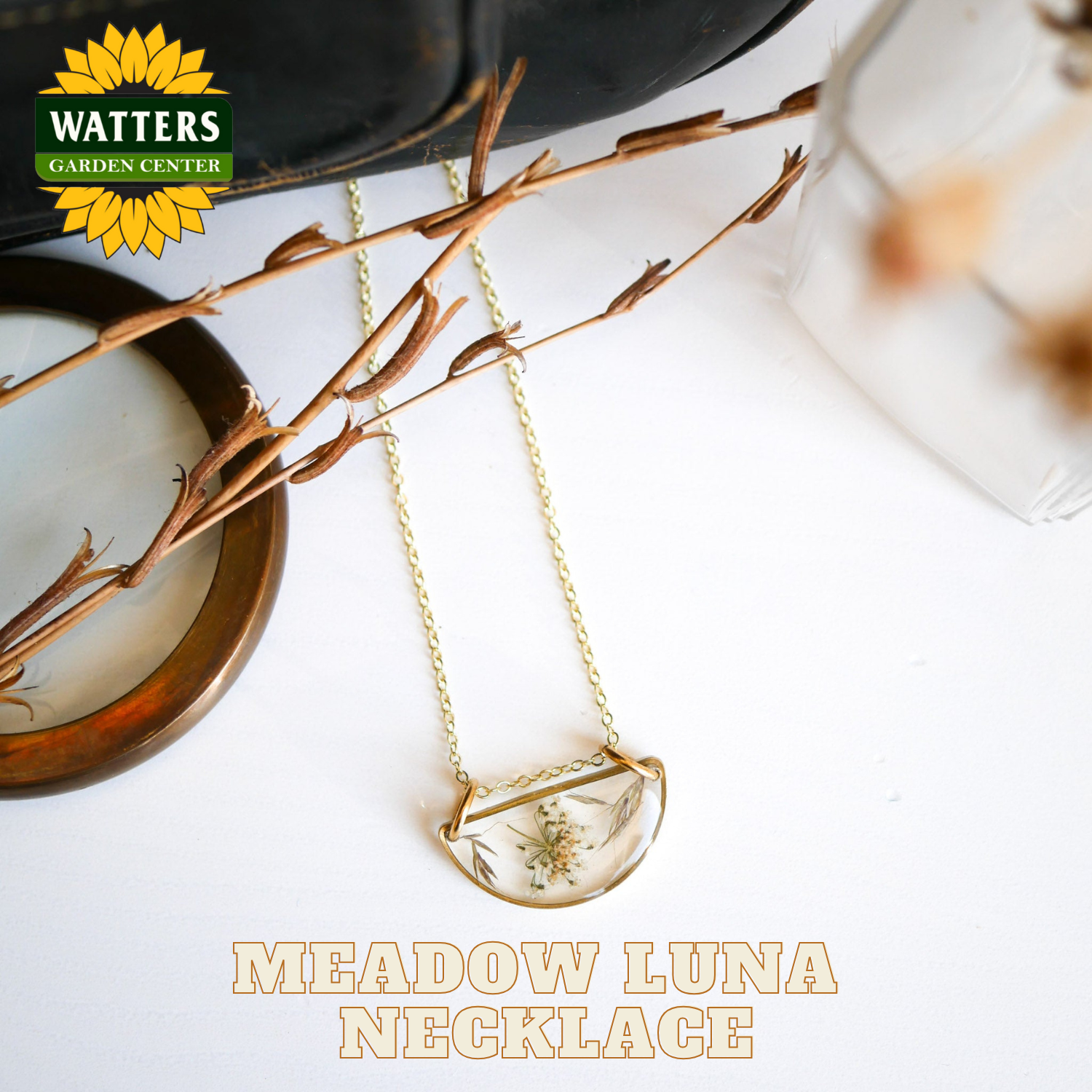 Gold necklace with a pendant on a white surface, featuring Watters Garden Center branding.