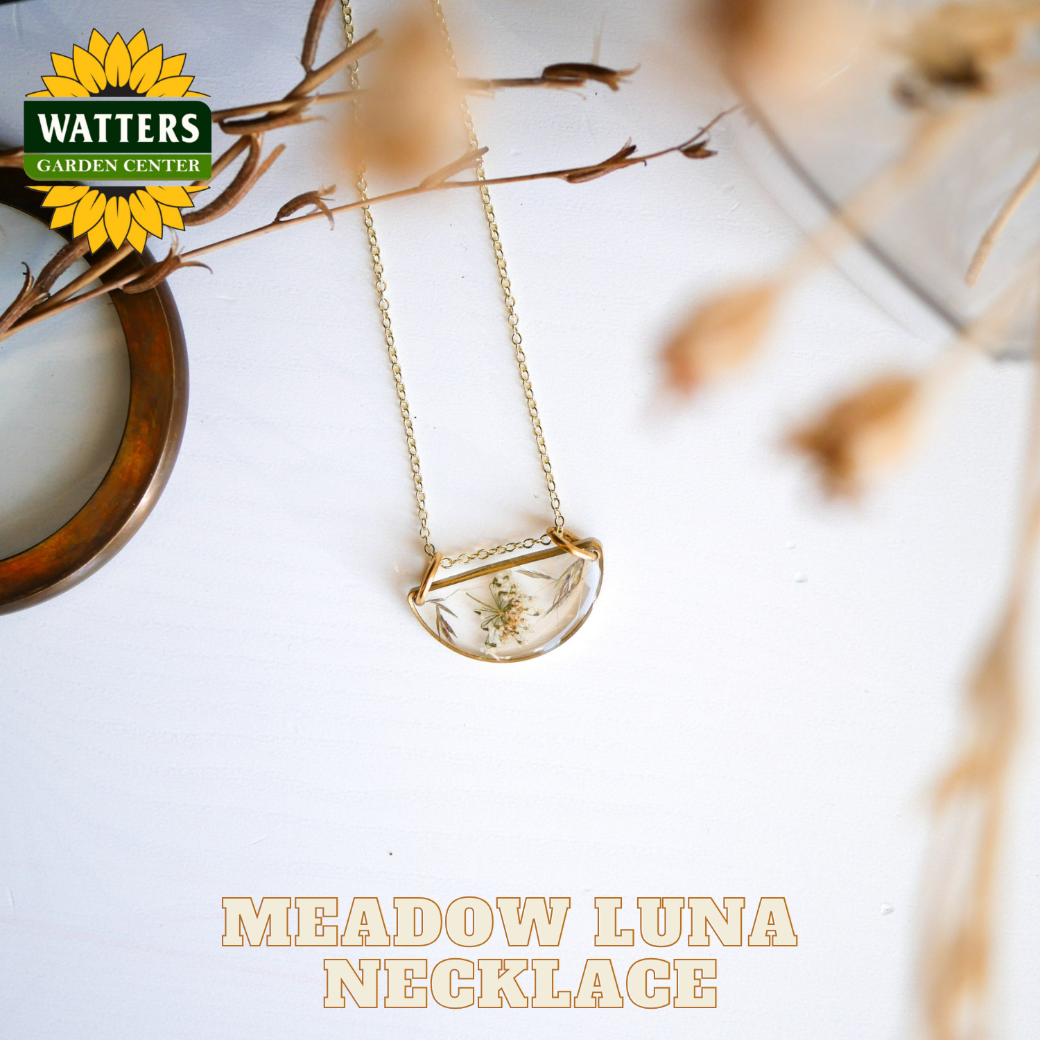 Gold necklace with a pendant on a white surface with 'Watters Garden Center' branding.