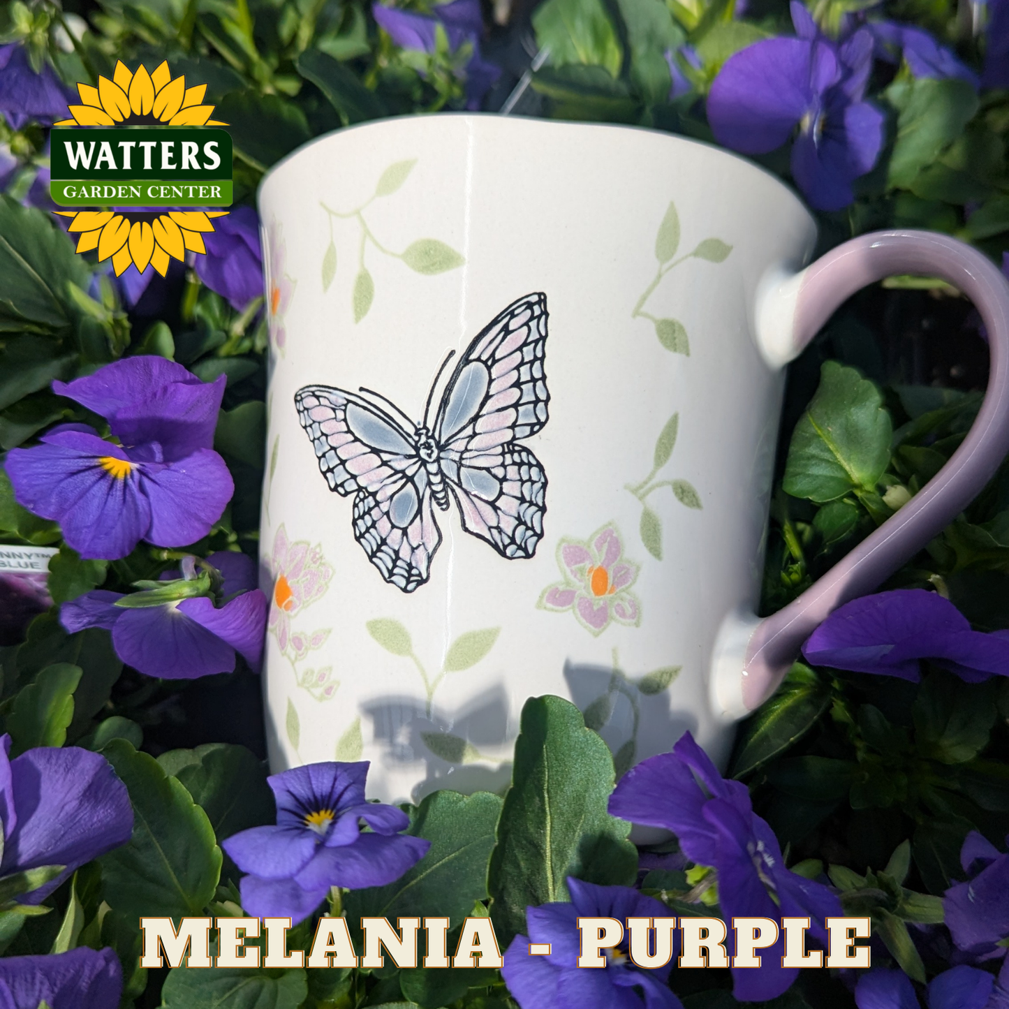 White mug with butterfly design in a bed of purple flowers, featuring Watters Garden Center logo.